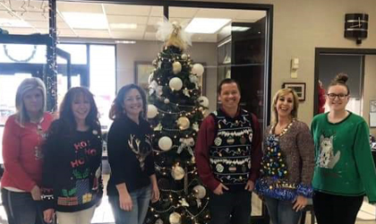 EUCCU employees in Christmas sweaters standing next to the Angel Tree.